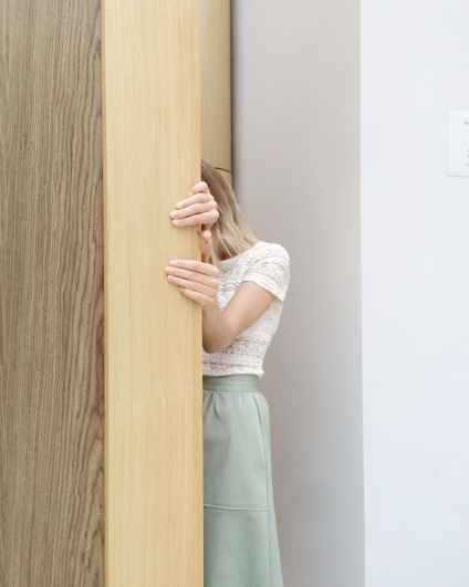 woman in white lace cap sleeved top and green skirt hiding behind brown wall